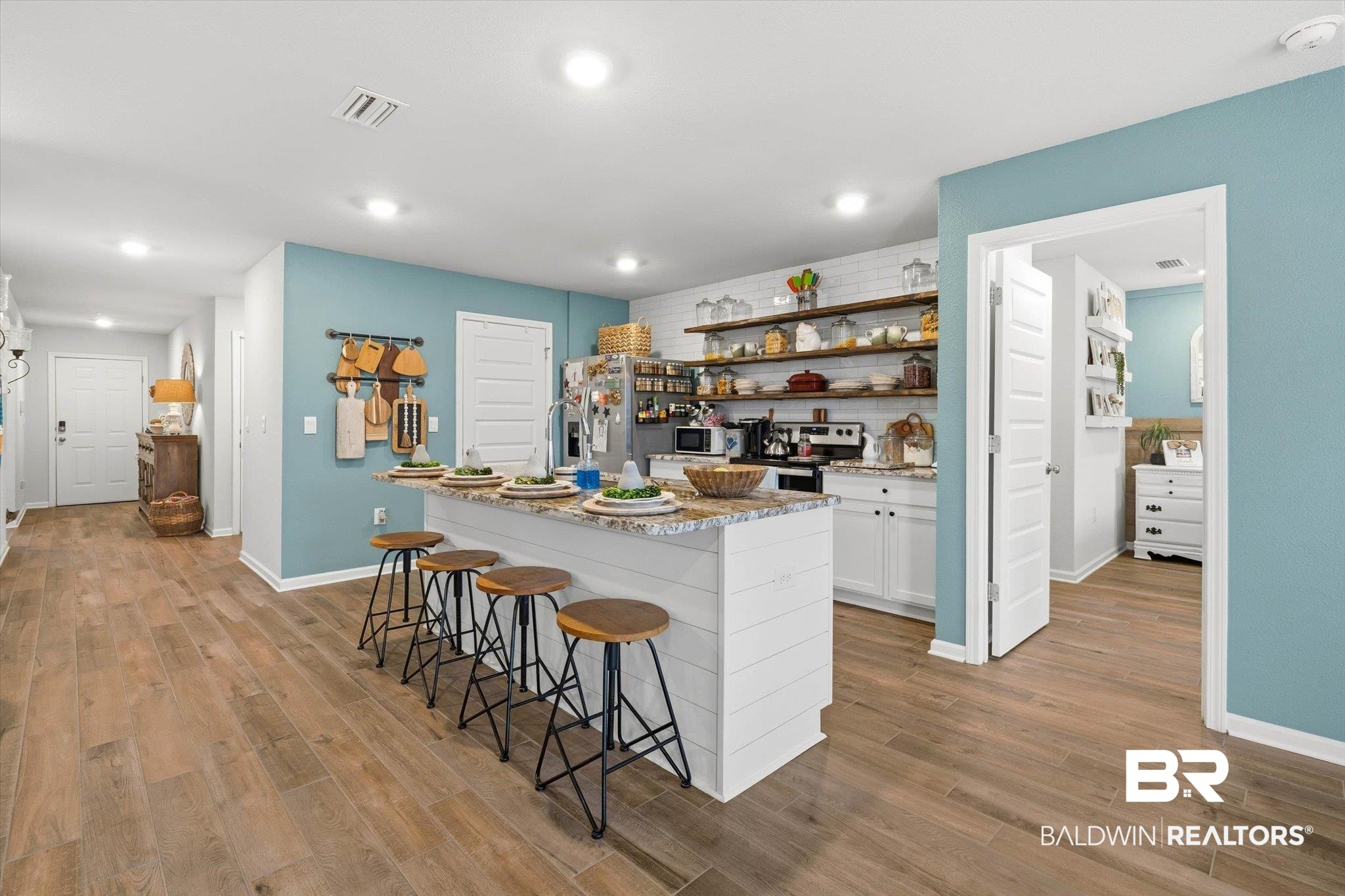 17041 Muse Street Loxley, AL 36551 - Photo 7 of 44 Kitchen featuring open shelves, white cabinets, a breakfast bar area, light stone countertops, and a kitchen island with sink