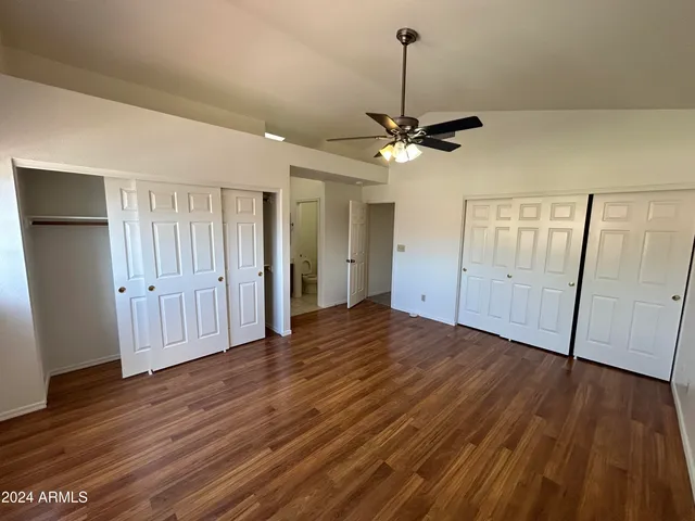 a view of an empty room with wooden floor ceiling fan