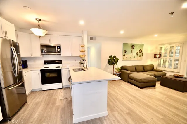 a large kitchen with stainless steel appliances kitchen island granite countertop a refrigerator a stove top oven a sink dishwasher and white cabinets with wooden floor