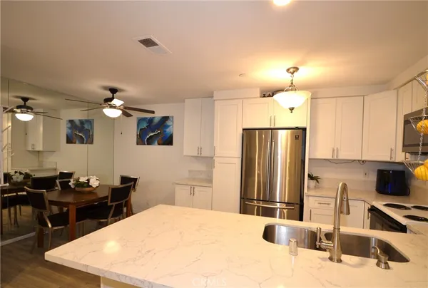 a kitchen with stainless steel appliances kitchen island granite countertop a sink dishwasher a refrigerator with wooden cabinets and floor