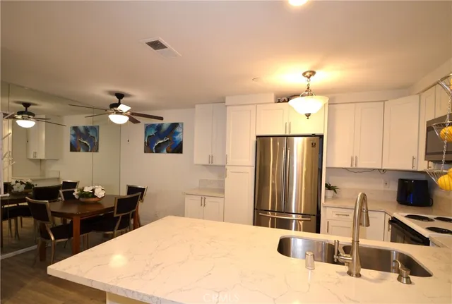 a kitchen with stainless steel appliances kitchen island granite countertop a sink dishwasher a refrigerator with wooden cabinets and floor