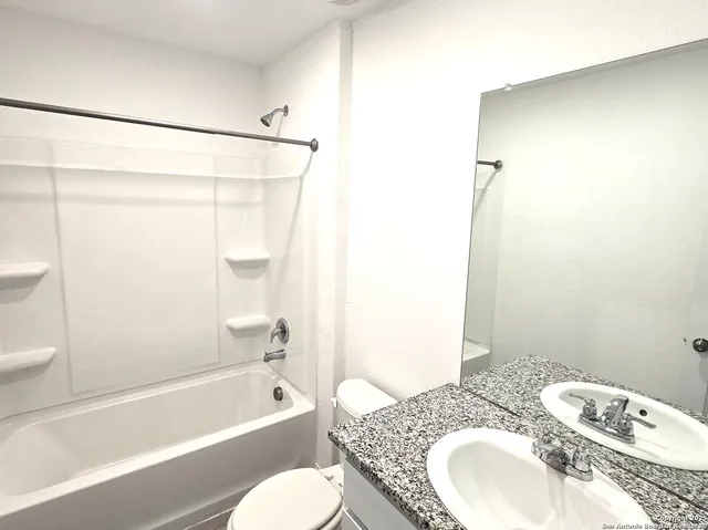a bathroom with a granite countertop bathtub sink vanity mirror and toilet