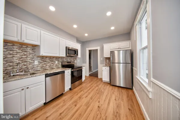 a kitchen with granite countertop wooden floors a refrigerator and white cabinets