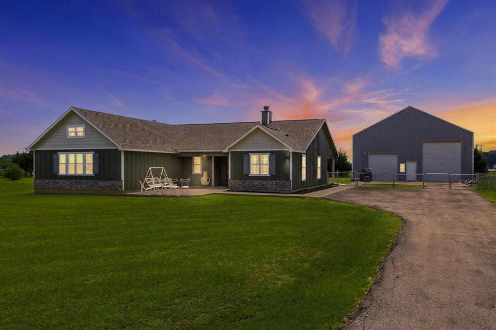 Ranch-style residence featuring a dark green vertical siding exterior, stone accents, and a grey shingle roof