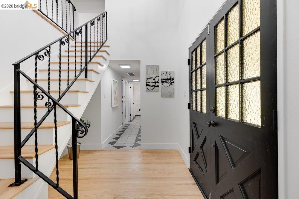 1298 Ribbon Street Foster City, CA 94404 - Photo 15 of 86 Entryway featuring a black double door with textured glass panels, light wood-finish flooring, a white staircase with black wrought iron railing, and a hallway with geometric tile flooring