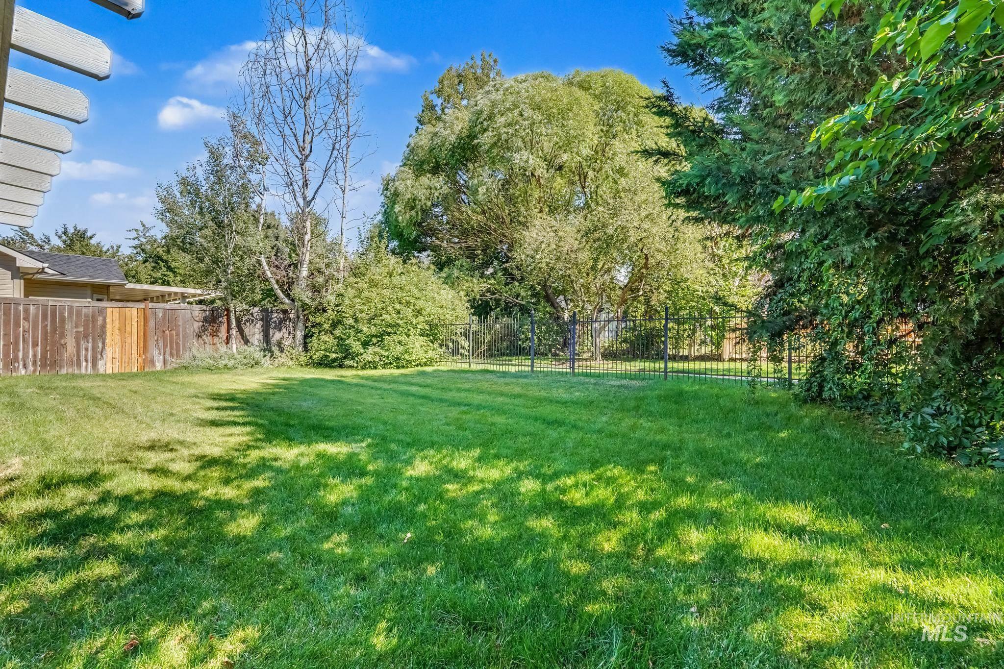 14421 West Stockwell Street Boise, ID 83713 - Photo 20 of 20 Expansive green lawn surrounded by mature trees, a wood-panel fence, and a black metal fence
