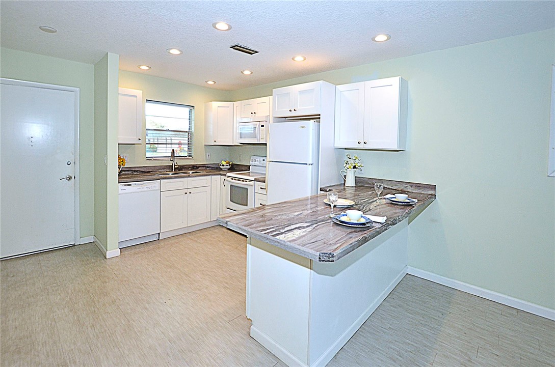 a kitchen with kitchen island a stove a sink a refrigerator and white cabinets with wooden floor
