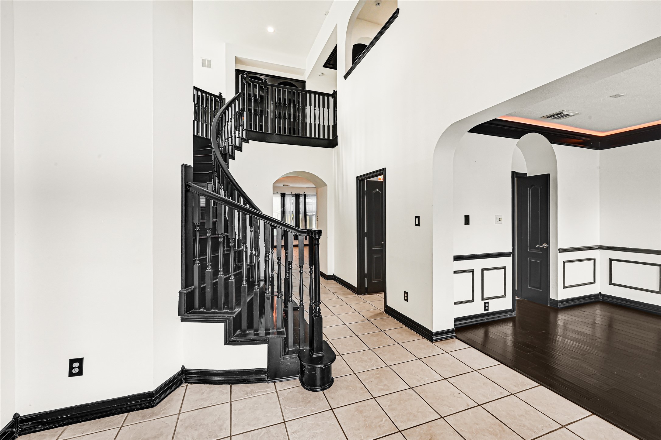 14714 Placid Point Humble, TX 77396 - Photo 9 of 37 This spacious home features a grand entryway with a dramatic curved staircase, high ceilings, and elegant dark trim accents. The open layout offers a mix of tile and wood flooring, with archways connecting rooms, creating a luxurious and welcoming atmosphere.