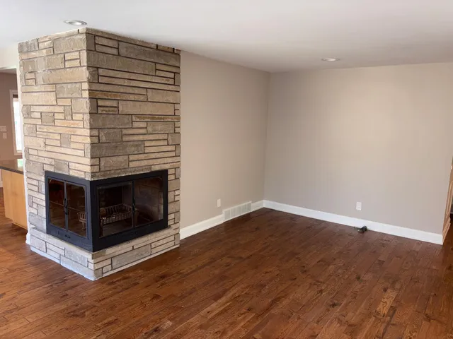 a view of an empty room with wooden floor and a fireplace