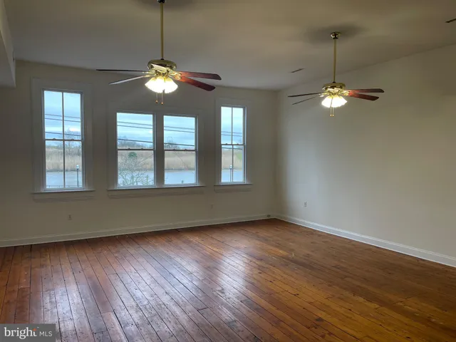 a view of a room with wooden floor ceiling fan and windows
