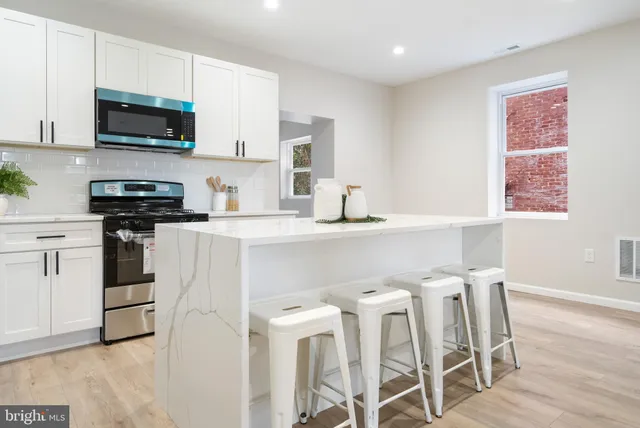 a kitchen with stainless steel appliances a stove a sink a microwave a refrigerator and white cabinets