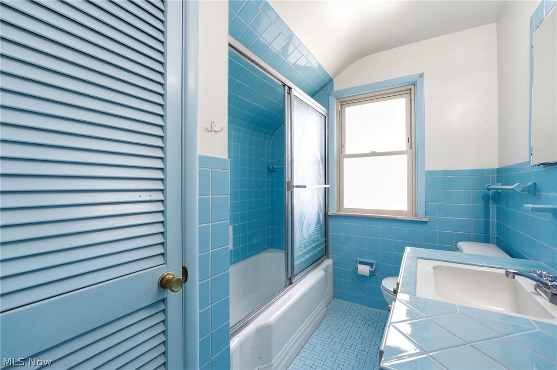 2537 Edgewood Road Beachwood, OH 44122 - Photo 30 of 39 Bathroom featuring a bathtub with a sliding glass door enclosure, a single vanity with a tiled countertop, a window with frosted glass, and blue wall and floor tiling