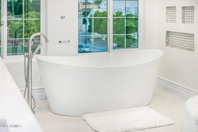 a view of a white house in front of a big yard with plants and large trees