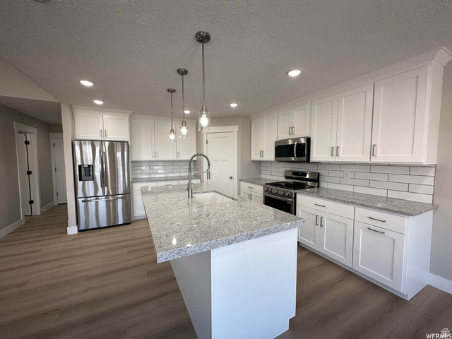 1171 West 2330 North Helper, UT 84526 - Photo 4 of 26 Kitchen with white cabinets, stainless steel appliances, dark wood-style flooring, light stone counters, and a textured ceiling