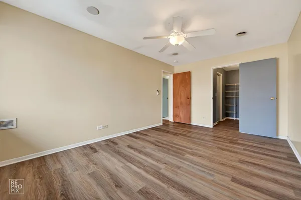 a view of an empty room with wooden floor and fan