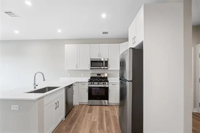 a kitchen with stainless steel appliances a sink a stove a refrigerator cabinets and a wooden floor