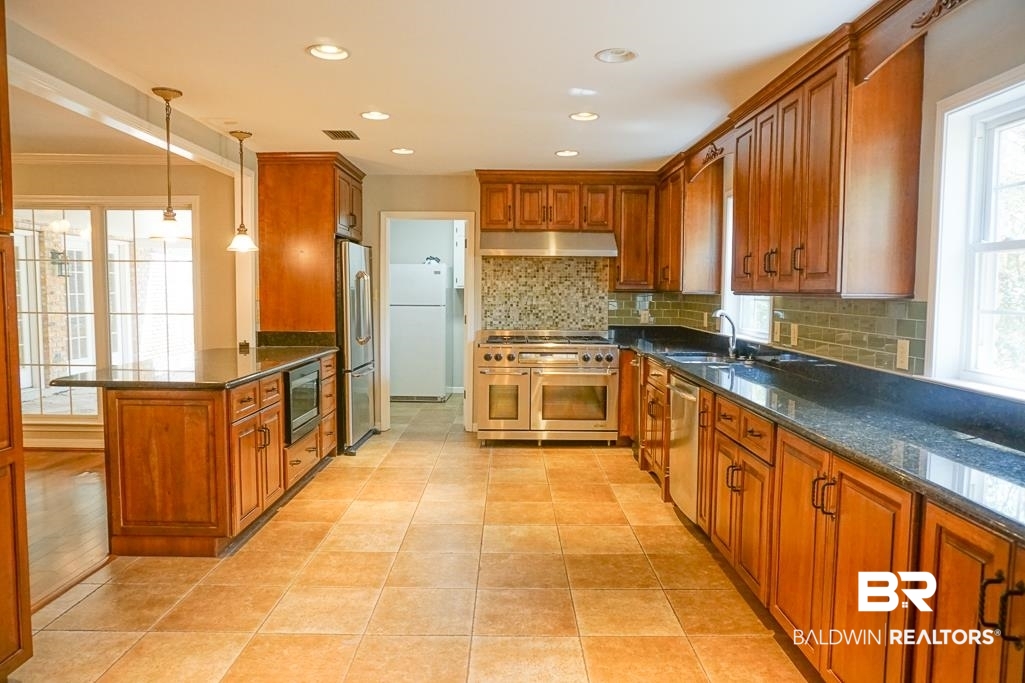 255 Suffolk Road Mobile, AL 36608 - Photo 9 of 29 Kitchen featuring dark stone counters, wood finish cabinetry, stainless steel appliances, a peninsula, and crown molding
