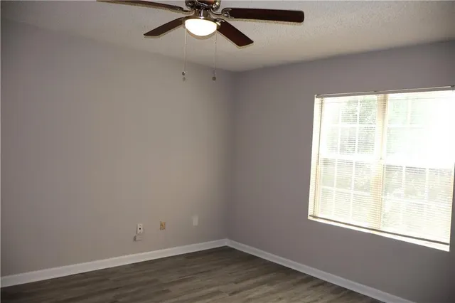 an empty room with wooden floor fan and windows