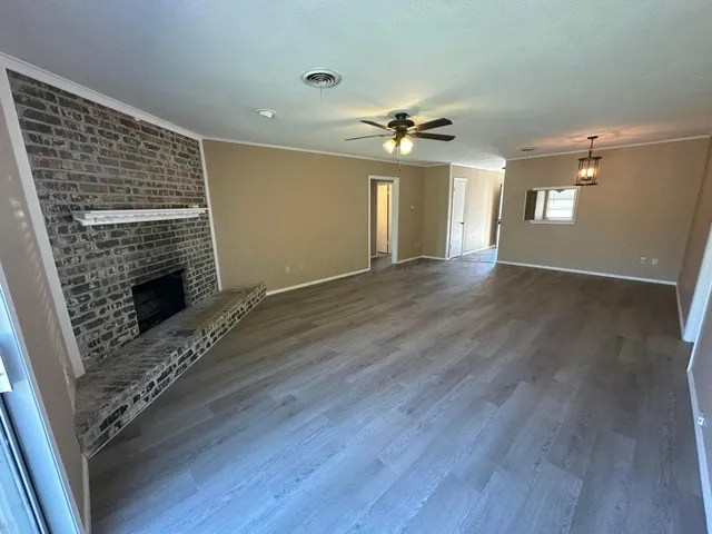 a view of an empty room with wooden floor fireplace and a window