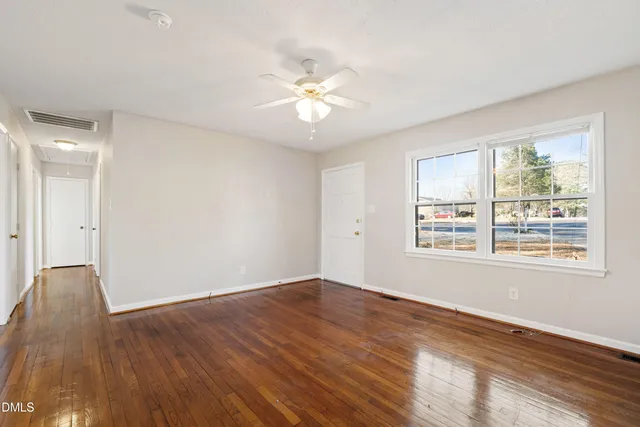 a view of an empty room with wooden floor and a window