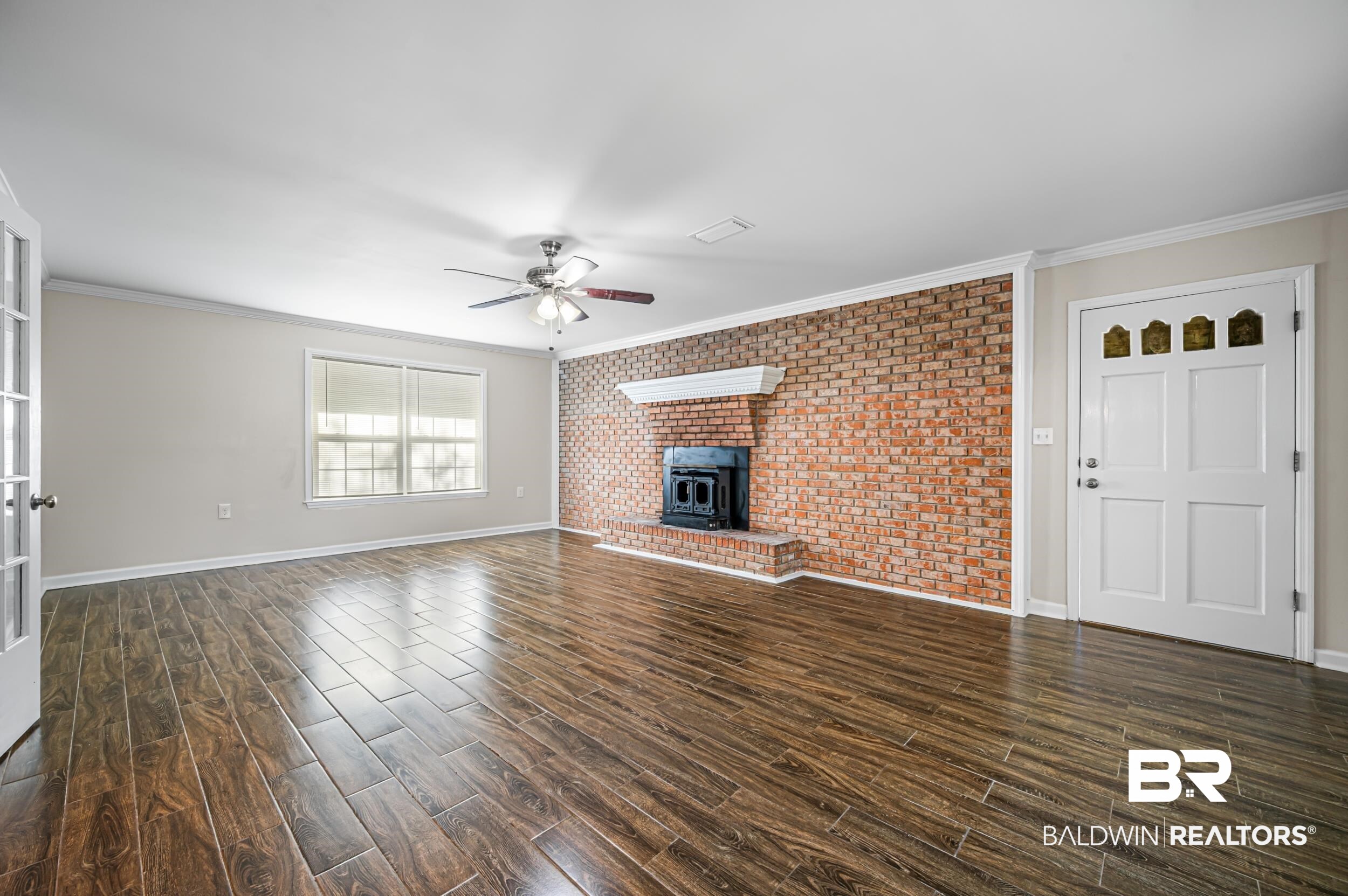 1605 Collier Avenue Bay Minette, AL 36507 - Photo 13 of 36 Unfurnished living room featuring ornamental molding, a wood stove, brick wall, dark wood finished floors, and a ceiling fan