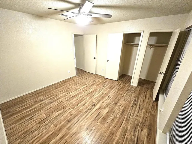 a view of an empty room with wooden floor and a ceiling fan