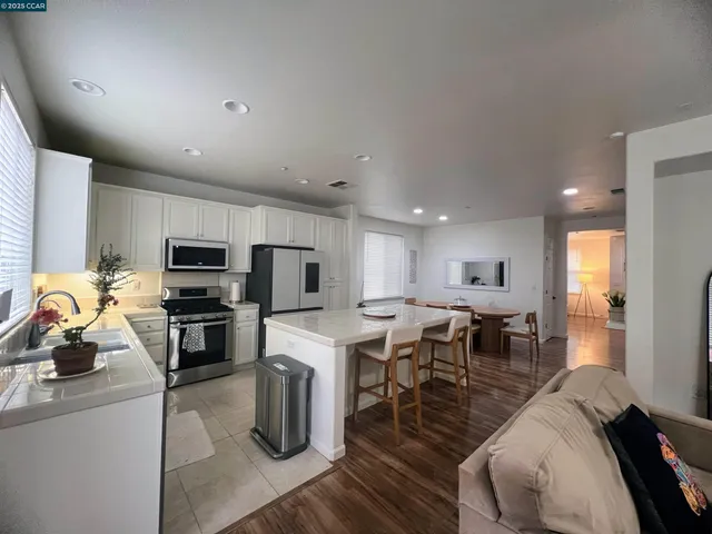 a kitchen with stainless steel appliances kitchen island granite countertop a stove top oven a sink a dining table and chairs with wooden floor