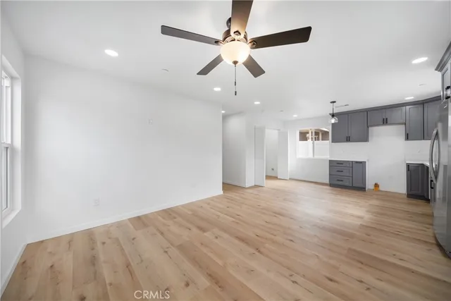 an empty room with wooden floor a ceiling fan and kitchen view