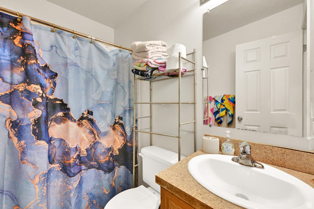 116 4th Street South Ogden, UT 84404 - Photo 6 of 7 Bathroom featuring a built-in vanity with a countertop and integrated sink, a wall-mounted mirror, and a toilet