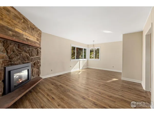 a view of an empty room with wooden floor fireplace and a window