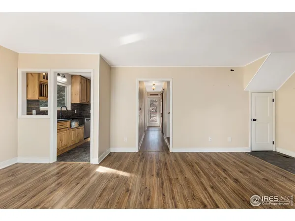 a view of an empty room with wooden floor and kitchen