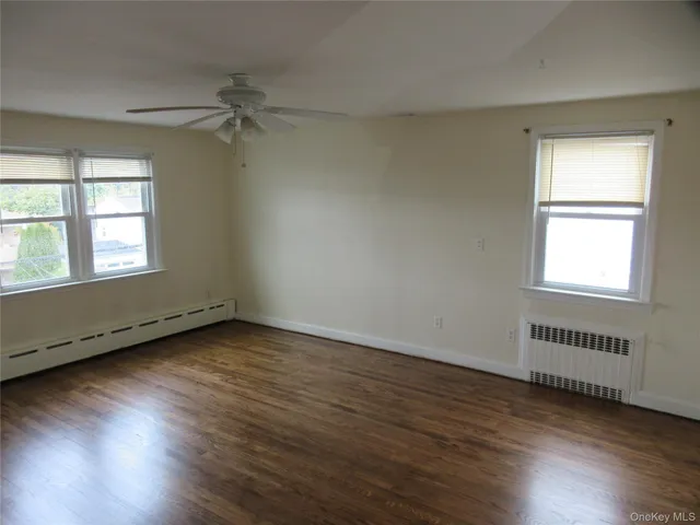 an empty room with wooden floor windows and fan