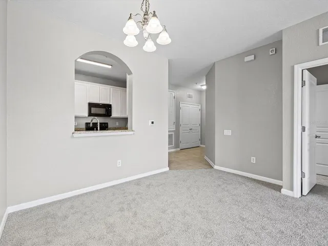 an empty room with a chandelier fan and kitchen view