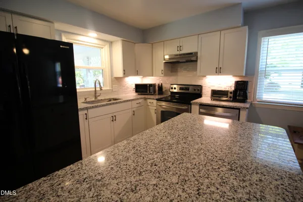 a kitchen with granite countertop a refrigerator stove top oven and sink