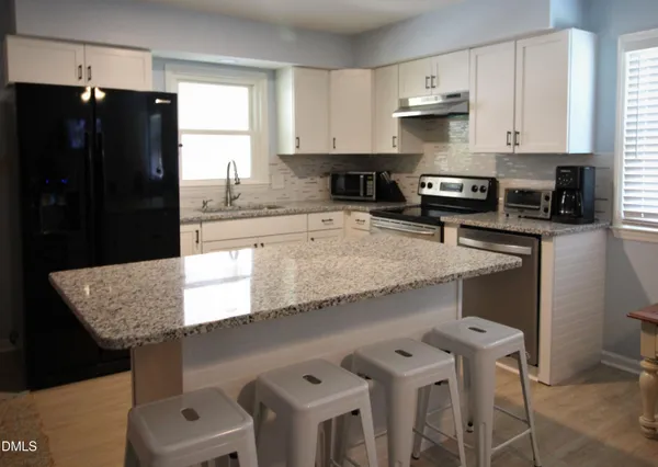 a kitchen with granite countertop a refrigerator a stove a sink dishwasher and white cabinets with wooden floor