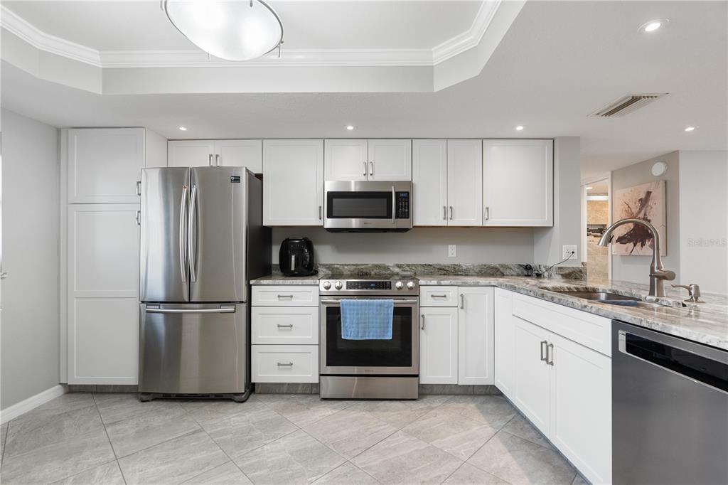 14001 Gulf Boulevard, Unit 201 Madeira Beach, FL 33708 - Photo 7 of 36 a kitchen with stainless steel appliances granite countertop a refrigerator a stove a sink and a microwave