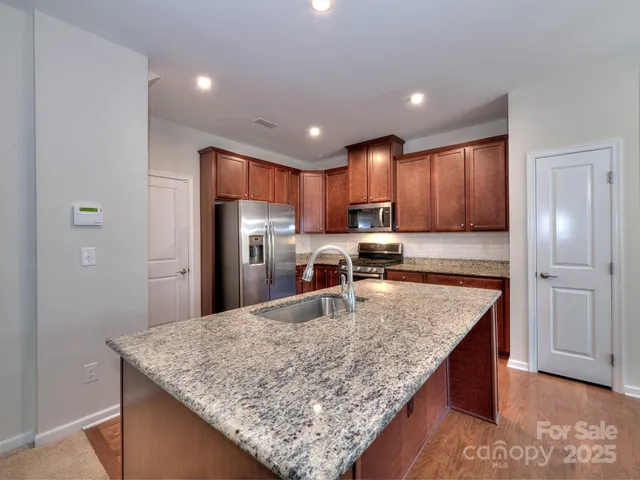 a kitchen with kitchen island granite countertop wooden cabinets refrigerator and microwave