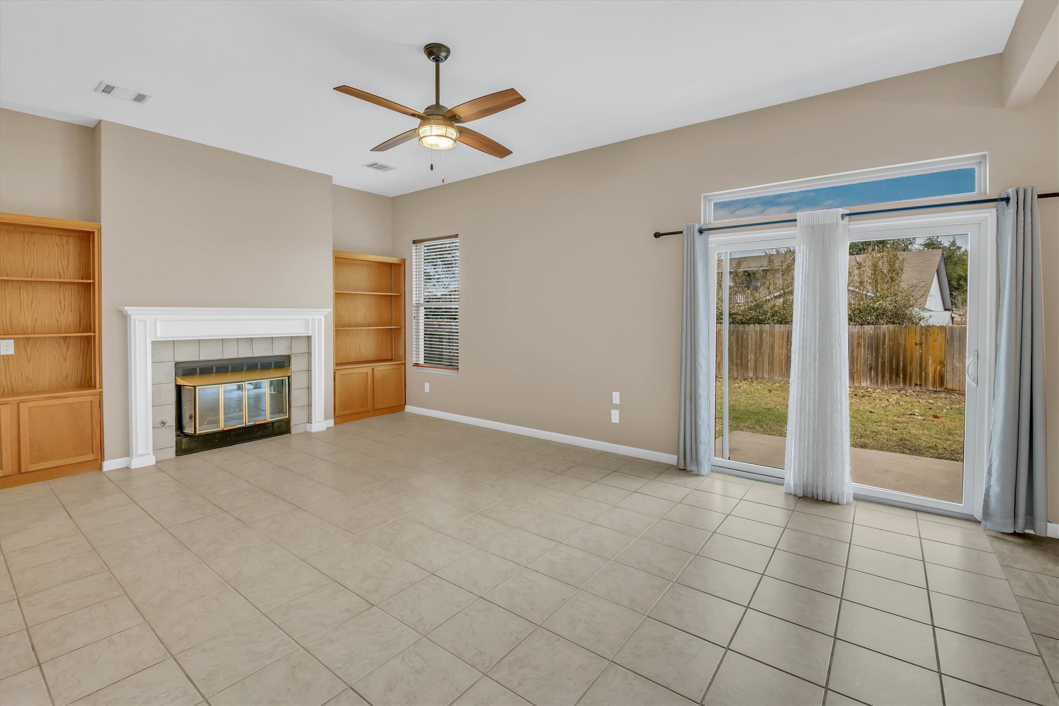 8108 Matchlock Cove Austin, TX 78729 - Photo 12 of 40 Unfurnished living room featuring built in shelves, ceiling fan, a tile fireplace, and light tile patterned flooring