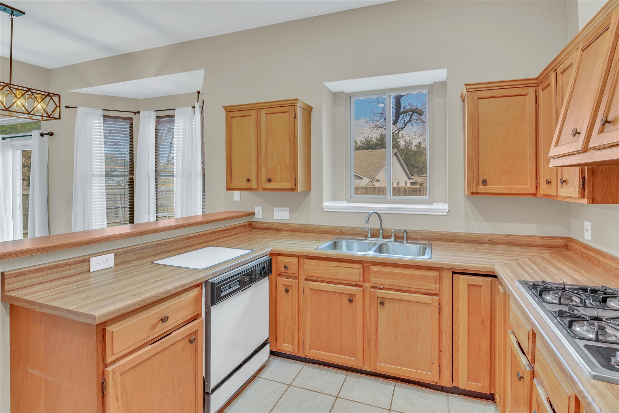 8108 Matchlock Cove Austin, TX 78729 - Photo 17 of 40 Kitchen featuring light wood finish cabinets, light countertops, a peninsula, dishwasher, and stainless steel gas stovetop