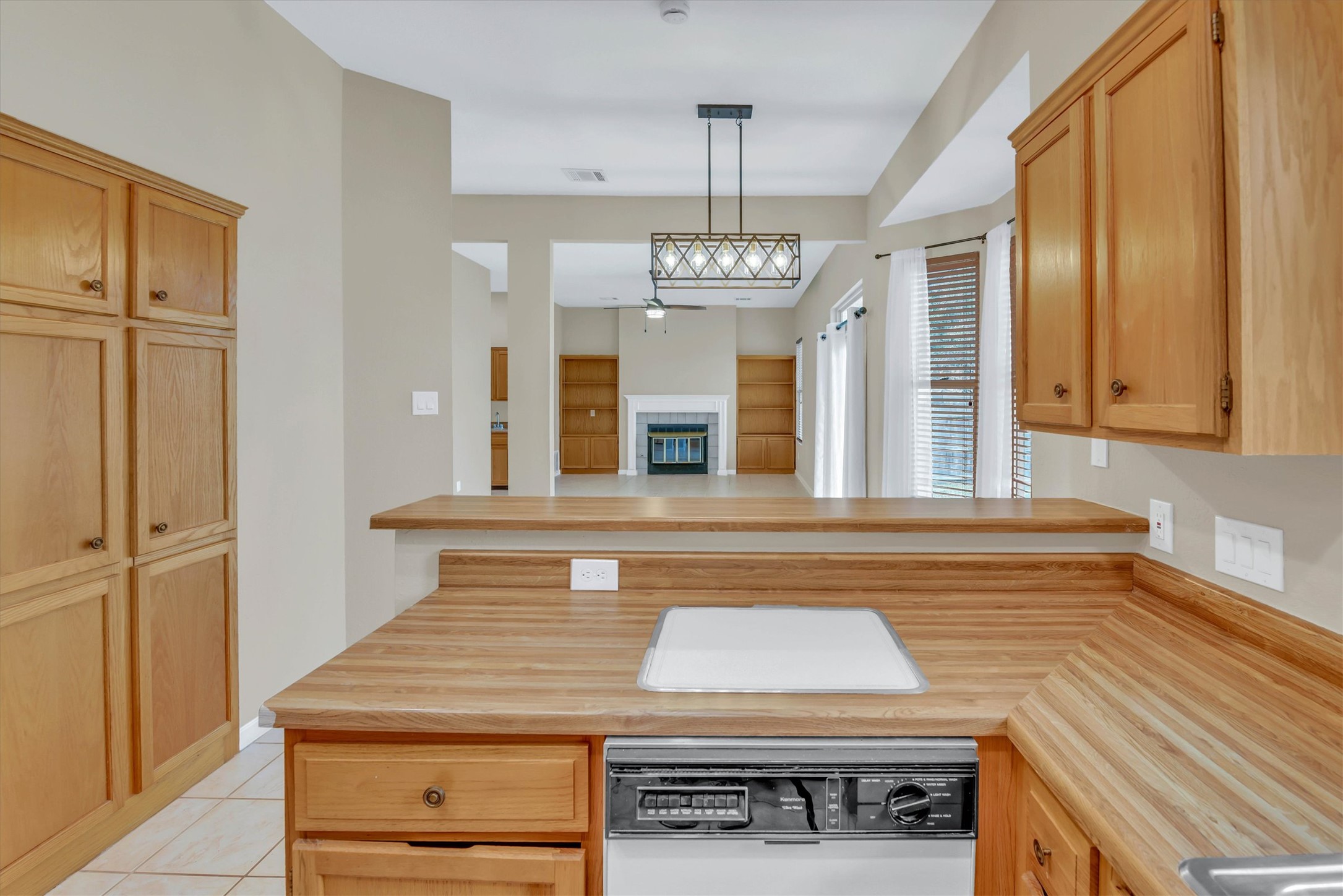 8108 Matchlock Cove Austin, TX 78729 - Photo 18 of 40 Kitchen featuring a peninsula, dishwasher, a glass covered fireplace, decorative light fixtures, and light wood finish cabinetry