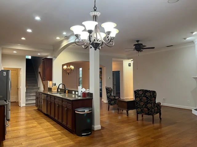a living room with couches chandelier and a dining table with wooden floor