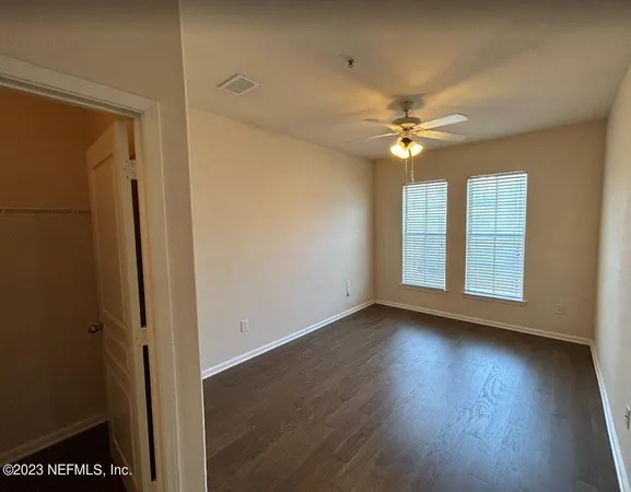an empty room with wooden floor fan and windows