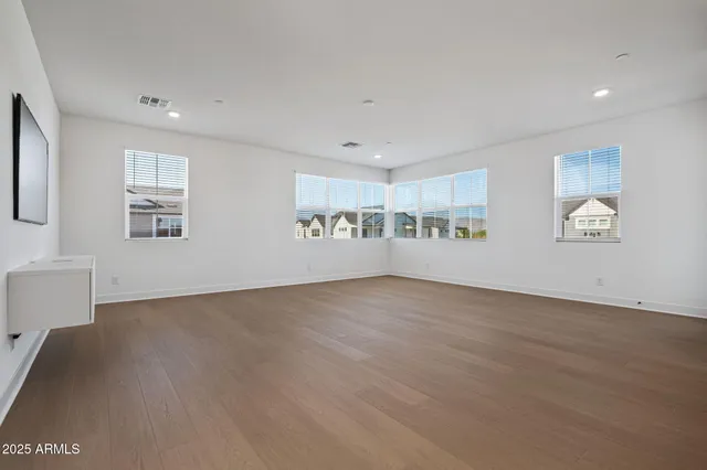 a view of an empty room with wooden floor and a kitchen