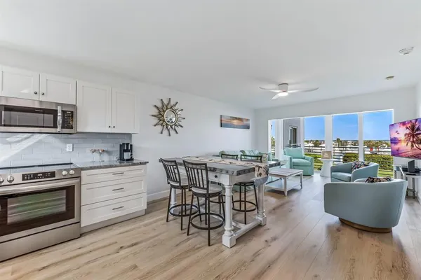 a living room with stainless steel appliances a dining table wooden floor and a view of kitchen