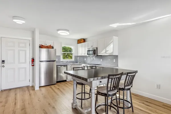 a kitchen with stainless steel appliances granite countertop a dining table chairs refrigerator and sink