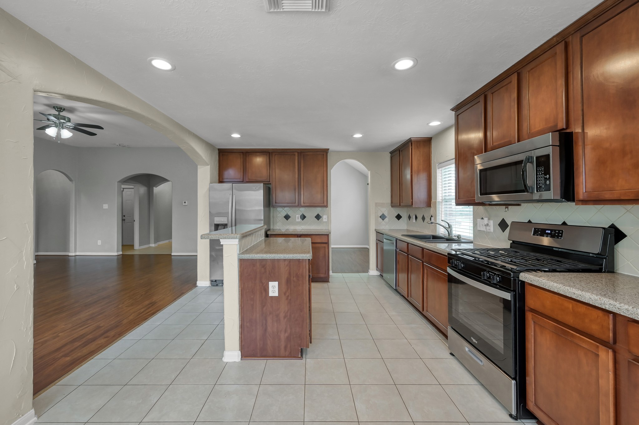 21331 Timber Pines Drive Spring, TX 77388 - Photo 8 of 22 A large island kitchen with raised breakfast bar provides additional seating while entertaining, or a spot for a quick meal before heading out for the day! Warm stained cabinets adorned with granite countertops, provide storage and prep space, plus classic black/stainless appliances including a recently installed gas range (2024) & a microwave (2024) offers the chef of the home all the modern conveniences!