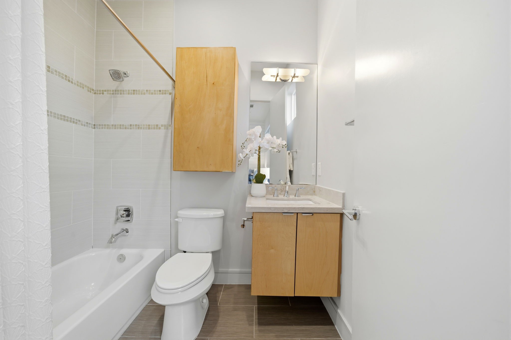 1405 Vermont Street, Unit A Houston, TX 77006 - Photo 35 of 46 Renovated secondary bath features a tub-and-shower combo with classic subway tile and a mosaic glass-tile inlay. Warm wood tones from the floating vanity and upper storage cabinet add a contemporary touch, while the quartz countertop and sleek rectangular sink provide a polished, luxury finish. Designer fixtures and a large vertical mirror maximize the airy atmosphere of this functional space.