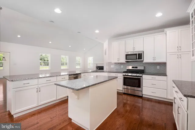 a kitchen with stainless steel appliances granite countertop a sink a stove a refrigerator and a oven with wooden floor