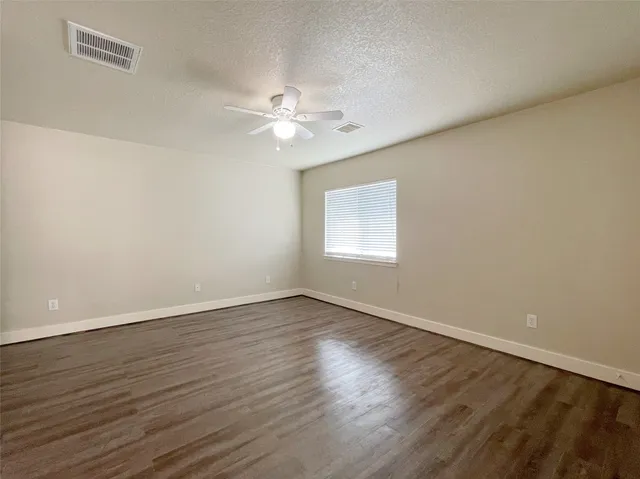 an empty room with wooden floor fan and windows