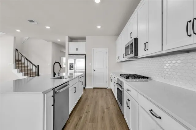 a kitchen with stainless steel appliances white cabinets a sink a stove a refrigerator and microwave